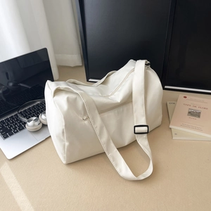 Minimalist large capacity white travel bag with shoulder strap next to a laptop and books
