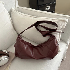 Minimalist burgundy half-moon shoulder bag with knotted strap on a white sofa