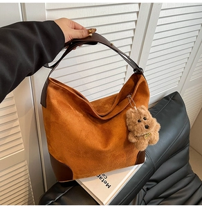 Detail of brown suede tote bag featuring leather straps and a cute plush bear charm