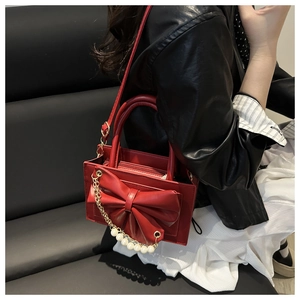 Détail d'un sac rouge avec grand nœud et chaîne de perles porté par un mannequin chic