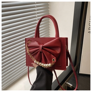 Détail du sac à main carré rouge avec grand nœud et chaîne décorative en perles blanches