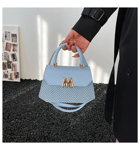 Light blue underarm bag featuring herringbone fabric detail and golden M clasp