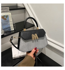 Close-up of black herringbone fabric handbag with gold M-shaped metal lock detail