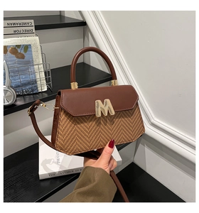 Detail of two-tone woven handbag with leather flap and gold M-logo on a bookshelf
