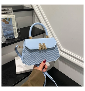 Detail of light blue crossbody bag featuring woven texture and gold M metal buckle hardware