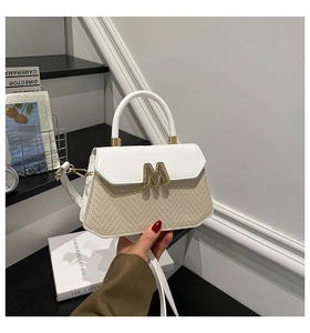 Detail of white leather and beige straw patchwork bag with golden M metal buckle