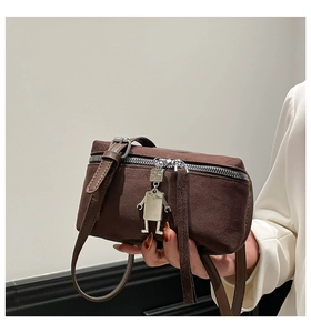 Detail of a brown suede crossbody bag featuring a silver robot pendant and metal zipper