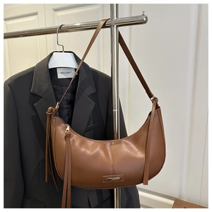 Détail d'un sac hobo en cuir marron avec pompon et boucle métallique sur cintre