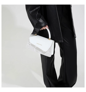 Detalle de un bolso bandolera blanco con motivos de letras sobre modelo con abrigo negro