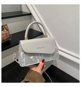 Detalle de bolso bandolera gris claro con estampado geométrico y letras doradas