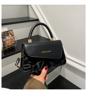 Detalle de bolso bandolera negro con logotipo dorado y textura de jacquard elegante