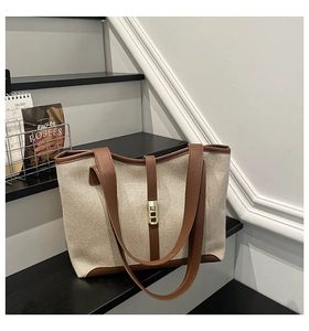 Detail of canvas tote bag featuring brown leather trim and a golden metallic buckle closure