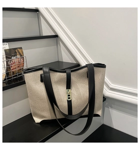 Close-up of canvas tote bag showing beige woven texture, black leather trim and gold lock