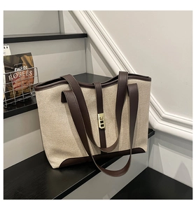 Detail of beige canvas tote bag with brown leather trim and golden metal clasp lock
