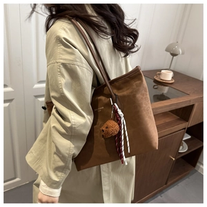 Detail of a large brown suede tote bag with a cute plush bear charm and brand logo