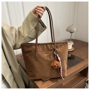 Close-up of brown suede tote bag with gold lettering and cute plush dog charm