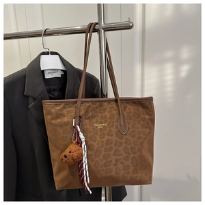 Detail of leopard print suede tote bag with golden logo and plush bear charm accent