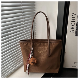 Detail of leopard print tote bag featuring plush teddy charm and woven rope decoration