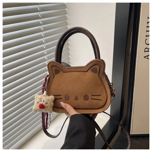 Detail van schattige bruine suède handtas in katvorm met gezichtsborduurwerk en pluche hanger