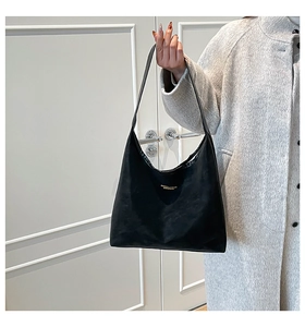 Detail of a minimalist black suede shoulder bag with gold lettering held by a model