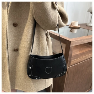 Detail of black leather crossbody bag with silver studs and heart-shaped metal accent