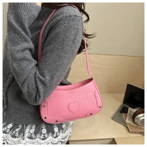 Detailed texture of pink crocodile pattern bag with heart patch and metal rivets