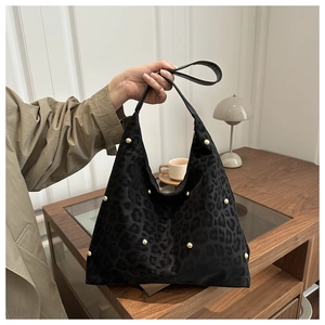 Detail of black leopard print tote bag with gold rivets held by model in trench coat