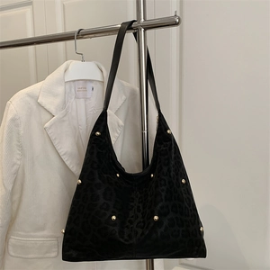Chic black leopard print tote bag with gold rivets hanging by a white corduroy jacket