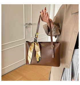 Detail of a brown leather tote bag with a floral silk scarf and gold metal buckle