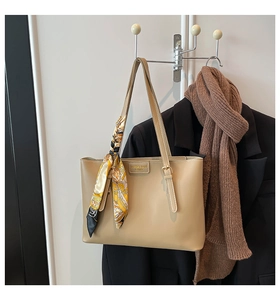 Detail of beige tote bag with a vintage silk scarf and metal logo on a studio background