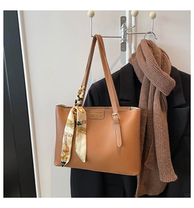 Detailed view of caramel tote bag with metal nameplate and silk scarf on a hanger