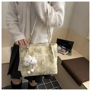 Detail of cream tote bag featuring star pattern, gold chain strap, and plush cloud charm