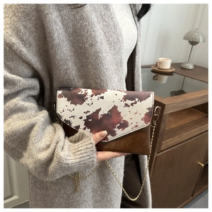 Detail of cow print envelope chain bag with polished gold strap in cozy interior