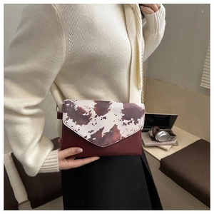 Detail of burgundy envelope bag with cow print flap and gold chain strap on shoulder