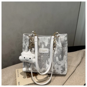 Detail of white star pattern tote bag with gold chain and cloud plush charm accessory