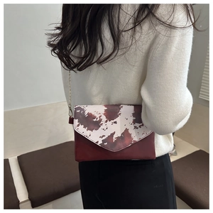 Detail of cow-print envelope bag with gold chain strap on model in ivory sweater