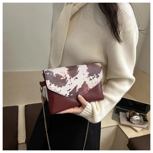 Detail of burgundy envelope bag with cow print flap and elegant gold chain strap