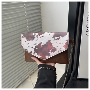 Detail of crossbody envelope bag showing cow print flap and golden chain strap texture