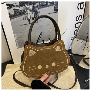 Nahaufnahme der katzenförmigen braunen Wildledertasche mit Ziernähten auf Strickuntergrund