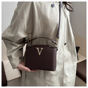 Close-up of golden V-shaped buckle on dark brown lychee leather bucket handbag