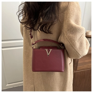 Detail of burgundy leather box bag with gold V-shape metal and adjustable shoulder strap