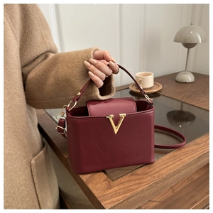 Close-up of wine red bucket bag with lychee texture and gold V-shaped metal buckle