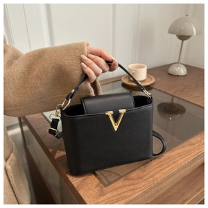 Detail of black pebbled leather bucket bag with gold V-shaped metal hardware on table