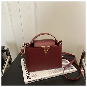 Close-up of wine red lychee grain leather bucket bag featuring a golden V-shaped metal logo