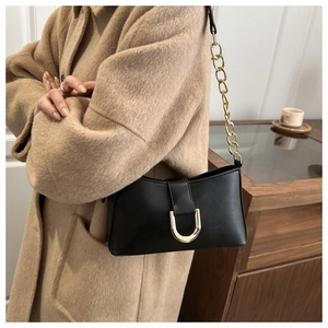 Détail du sac noir avec boucle en U dorée et bandoulière en chaîne métallique épaisse
