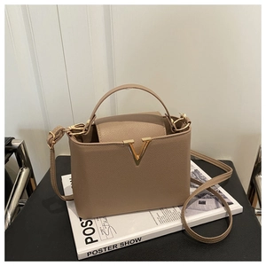 Detail of dark khaki bucket bag with golden V-shaped metal buckle on a magazine background
