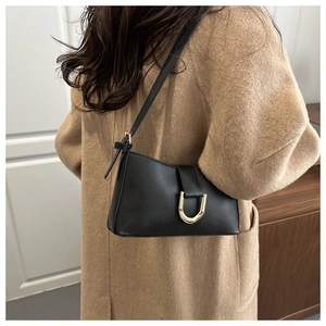 Détail du sac à bandoulière noir avec boucle dorée en fer à cheval sur un manteau en laine
