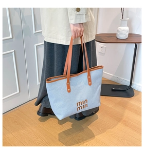 Detail of light blue woven tote bag featuring brown leather trim and stylish logo
