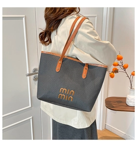 Detail of a woven tote bag with orange leather handles and embossed letters on side