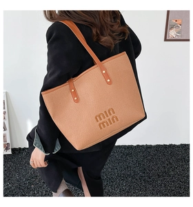 Detail of the woven tote bag with leather straps and logo held by a model